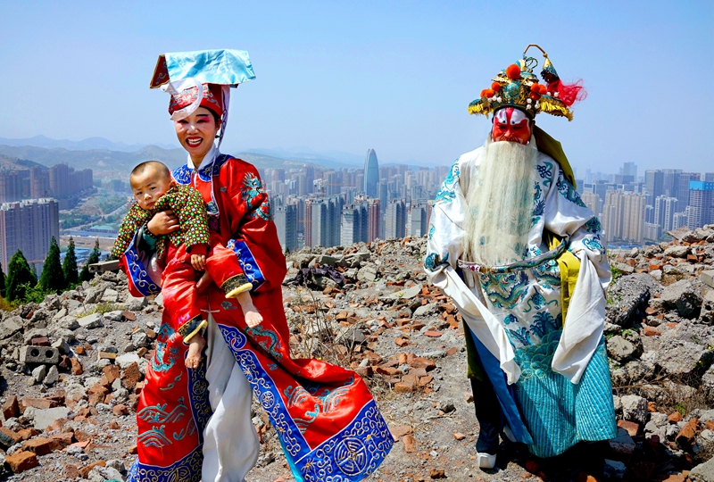 45 、《傳統與現代》2016年4月,濟南市漢峪金谷,來自魯西南的莊戶劇團演員抱著幼子趕場演出。艷麗的傳統戲服與腳下的瓦礫形成巨大反差,而他們身后的新城已經崛起,千年古城的時代氣息愈發濃郁。(呂廷川).JPG